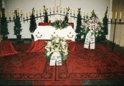 Trauerhalle. Weisser Sarg, roter Teppich und Kerzen.