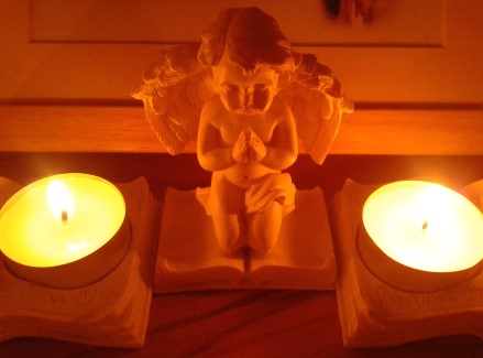 Kleiner betender Engel umgeben von Teelichtern vor Fotorahmen.